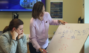 Two women looking at equation on white board