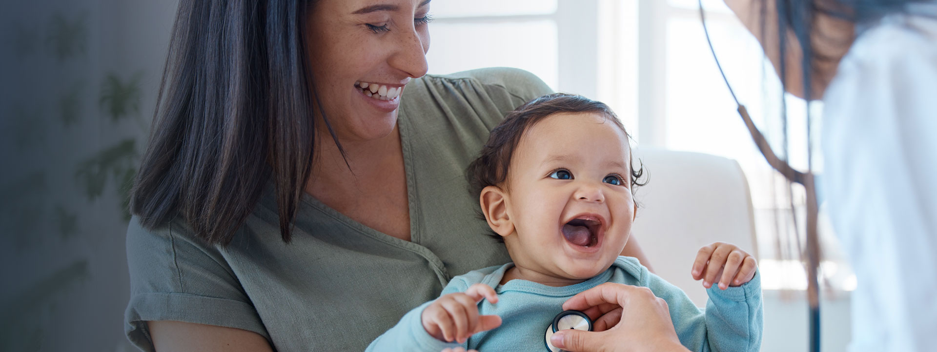 Infant on mom's lap with a doctor listening to chest using stethoscope