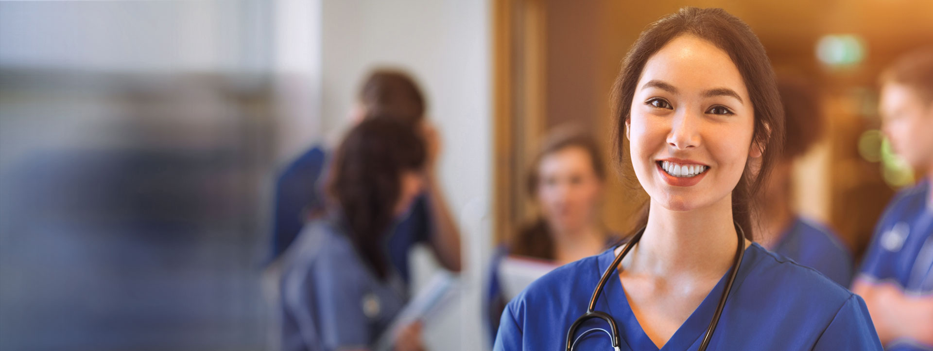 Woman in scrubs smiling at camera with group of medical professionals talking in the background